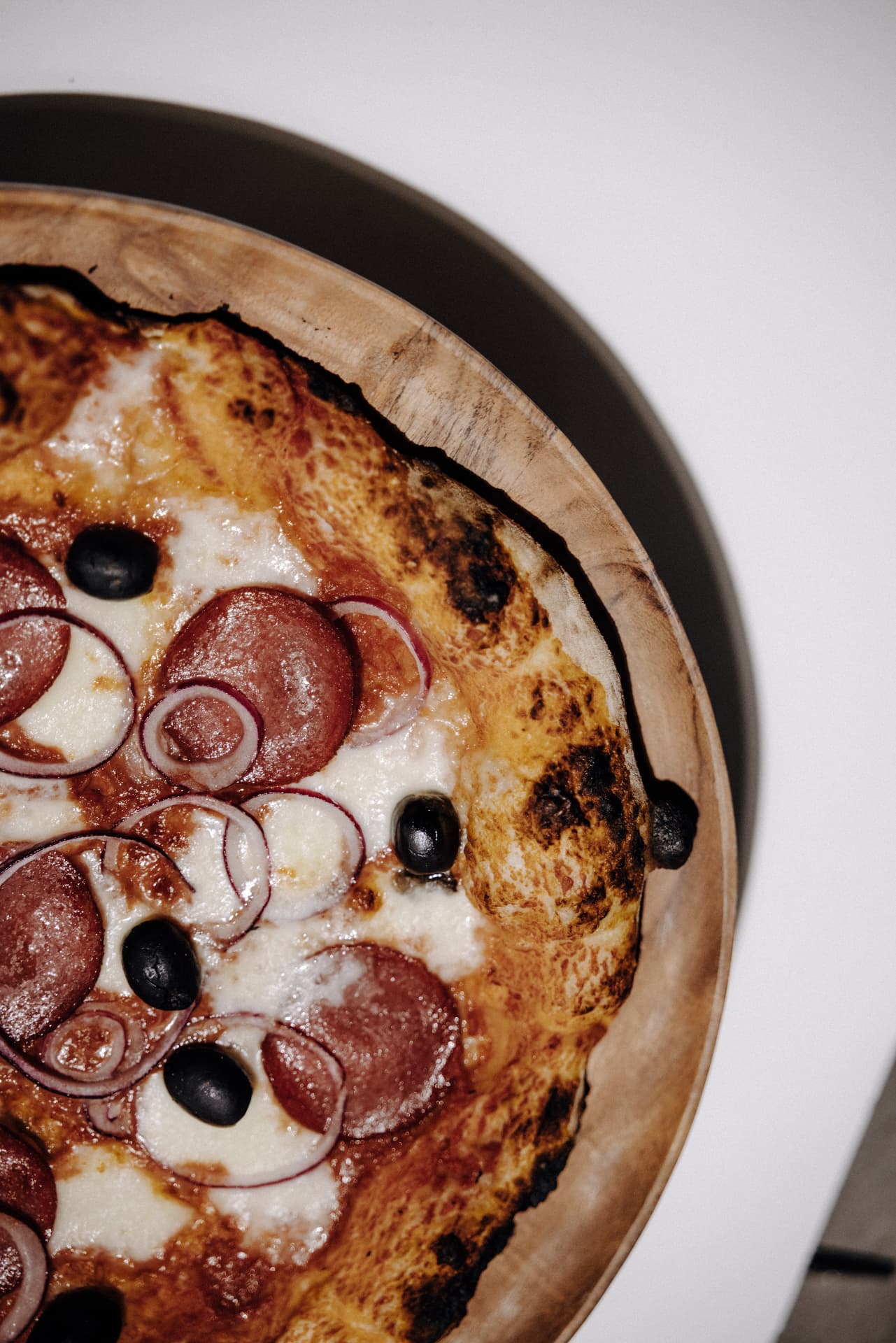 Frisch gebackene Pizza mit Salami, roten Zwiebeln und Oliven auf einem Holzbrett